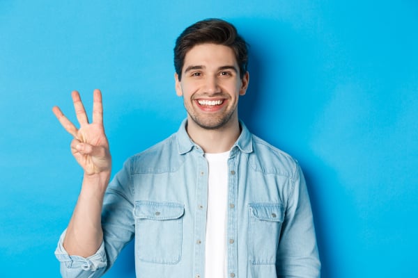 close-up-handsome-man-smiling-showing-fingers-number-three-standing-blue-background-1