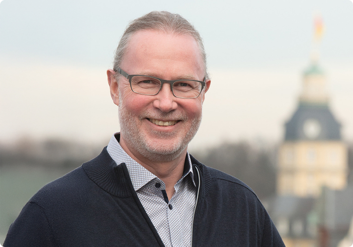 Mann mit Brille und grauem Haar trägt kariertes Hemd aus Baumwolle und dunkelblauen Pullover