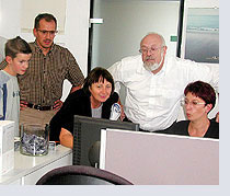 Fünf Personen arbeiten gemeinsam an Computern in einem Büro mit weißen Möbeln